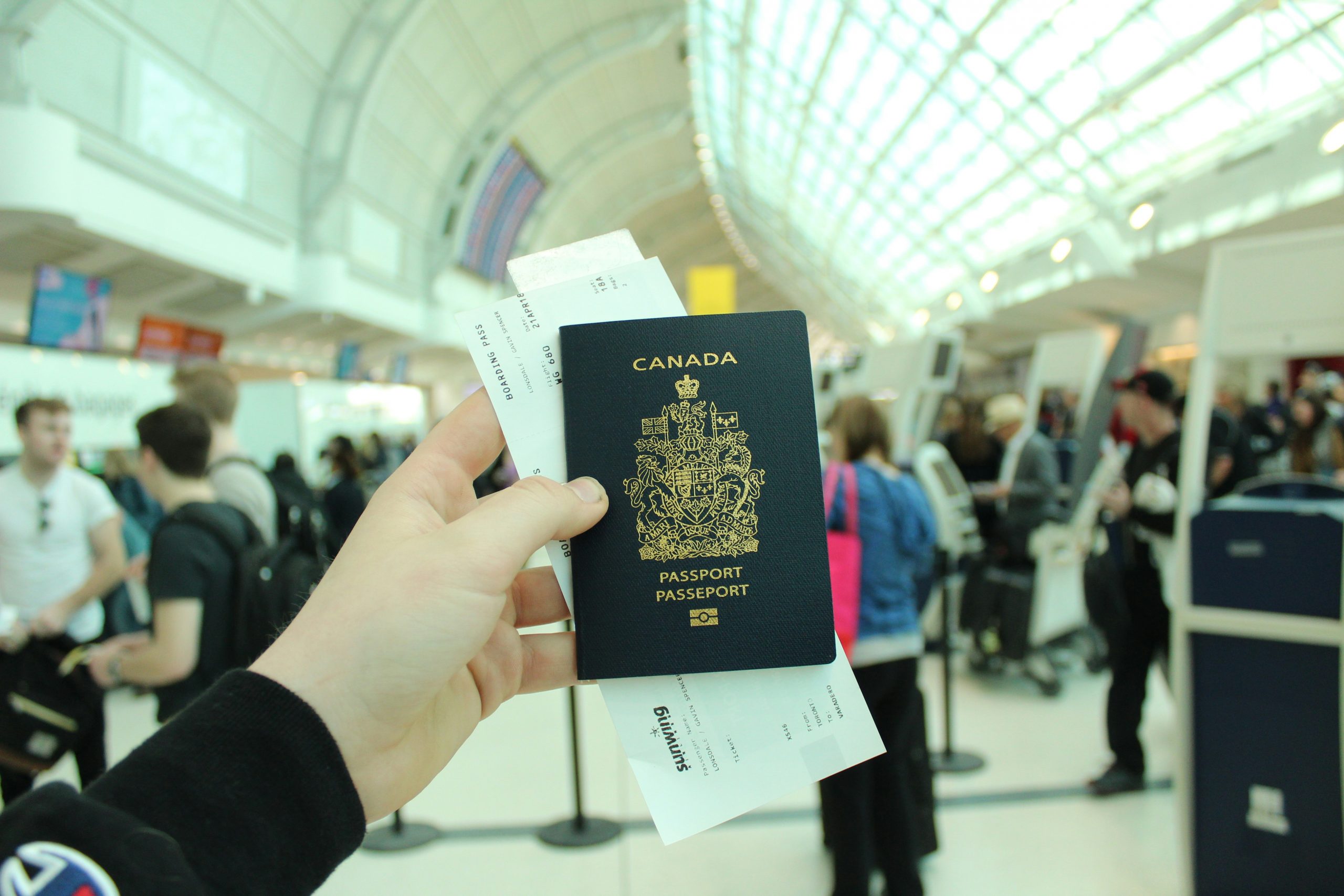 Canadian passport A hand holding a book titled "Canada Passport" at Toronto Pearson Airport, with travelers visible in the background.