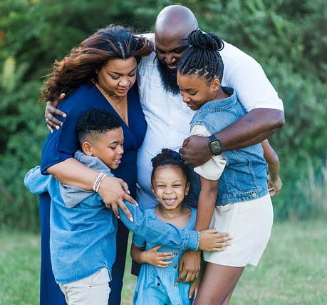 A family standing close together outdoors, embracing each other warmly, symbolizing unity and togetherness for Canada’s Family Sponsorship immigration program.